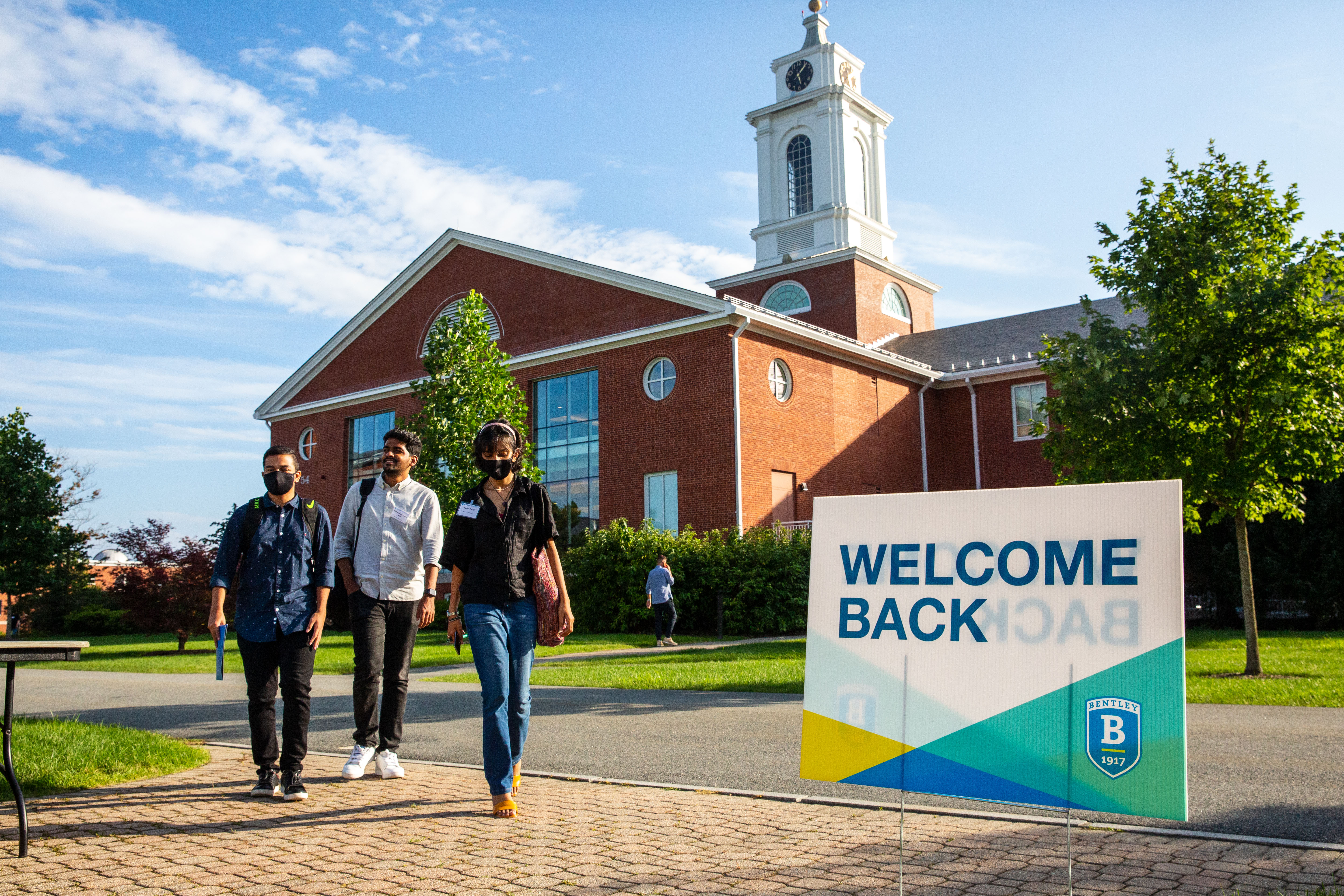 Students walking on campus near a sign saying Welcome Back
