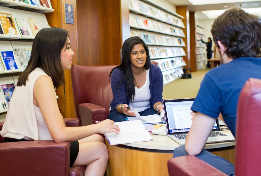 Two female students talk with a male student in the Bentley Library.