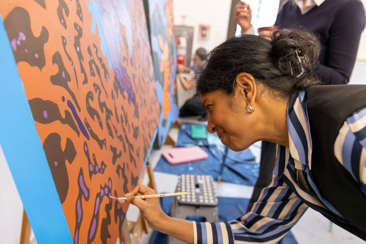 Neelangi Gunasekera, program manager of First-Generation presidential Fellows and Falcon Discovery Seminar at Bentley University, paints a mural during a collaborative art installation by Artist-in-residence Andromeda Lisle.