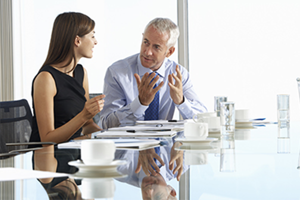 white man and women talking at table in corporate setting with documents in front of them 