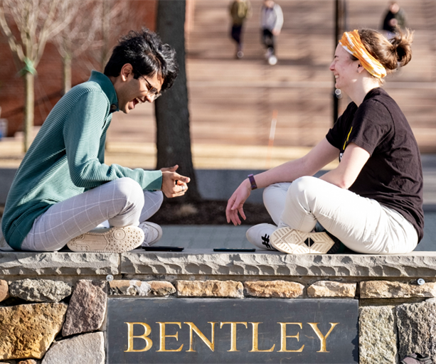 students sit on the Bentley campus sign