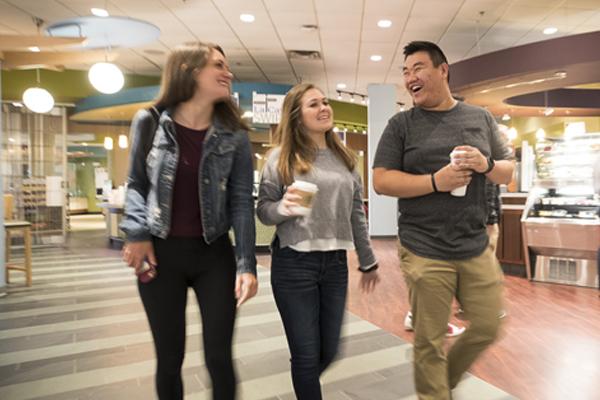 three students walk while drinking coffee and smiling