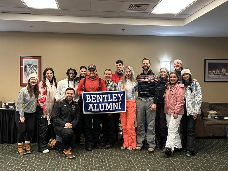 Bentley alumni take a group picture with a Bentley alumni banner inside a Killington property