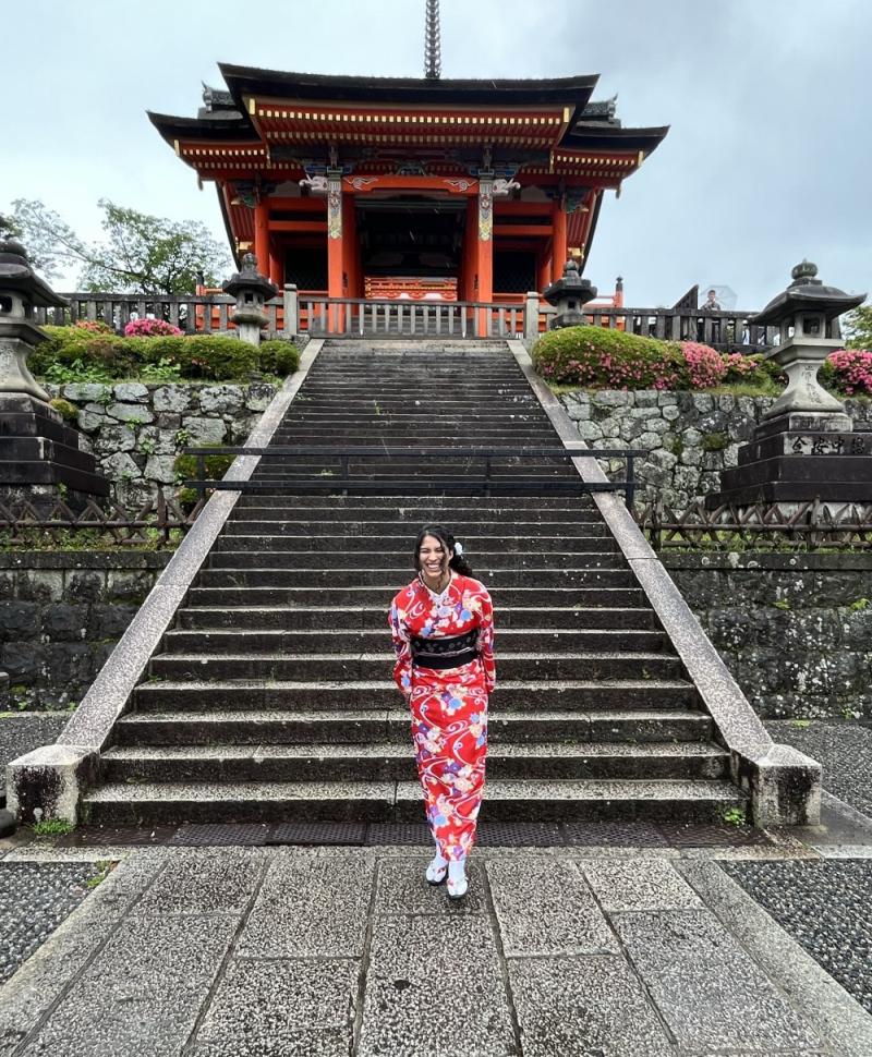 Photo of Bentley graduate student Isabel Maier, wearing a red kimono and black obi, standing at the base of a stone staircase leading to the Kiyomizu-dera Temple in Kyoto, Japan.