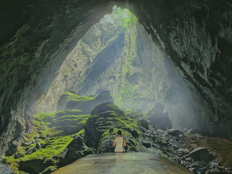 A person sits in the lotus pose, back to camera, within the otherworldly interior of Song Doong Cave in Vietnam.