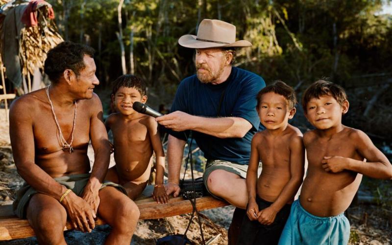 Dan Everett sits with members of the Pirahã, an indigenous tribe in the Brazilian rain forest. He holds a microphone to record the speakers' language. 
