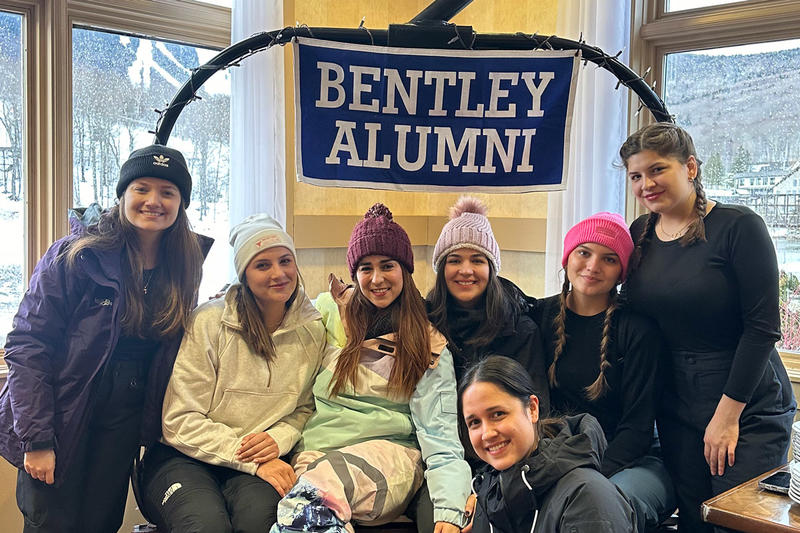 Alumni smiling in front of a Bentley Alumni banner